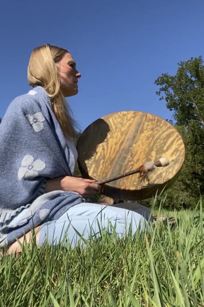 Jana Schulz spielt ihre schamanische Trommel auf einer Wiese